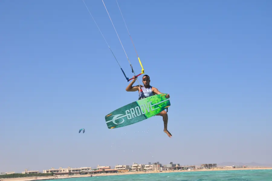 Kitesurfer in mid-air holding the bar, with the Marsa Alam shoreline and resort buildings behind