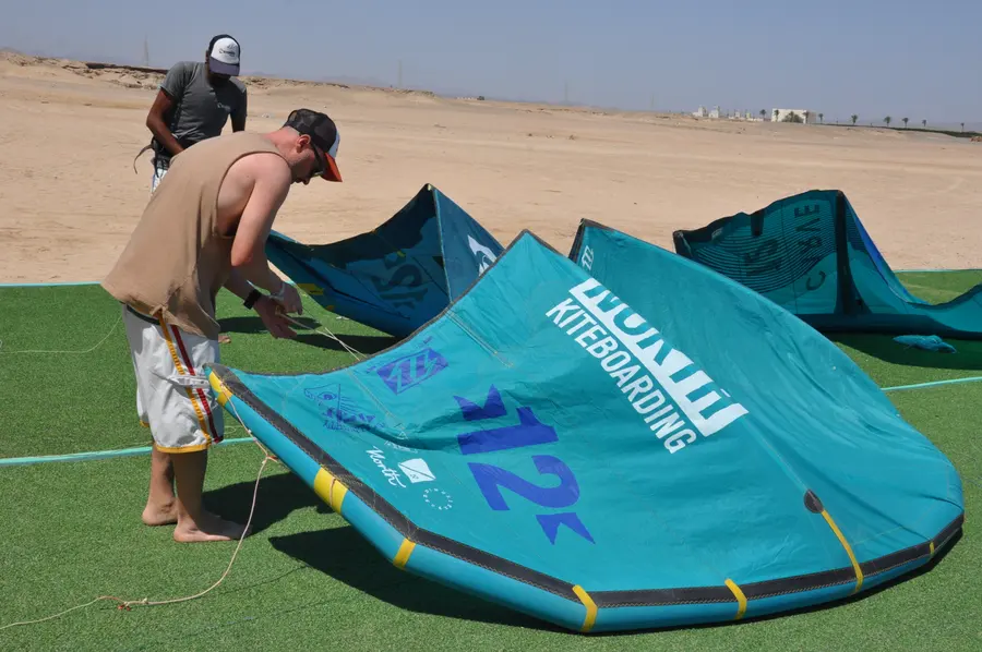 Two men preparing a large teal kite on the green mat at the KiteMood base in Marsa Alam